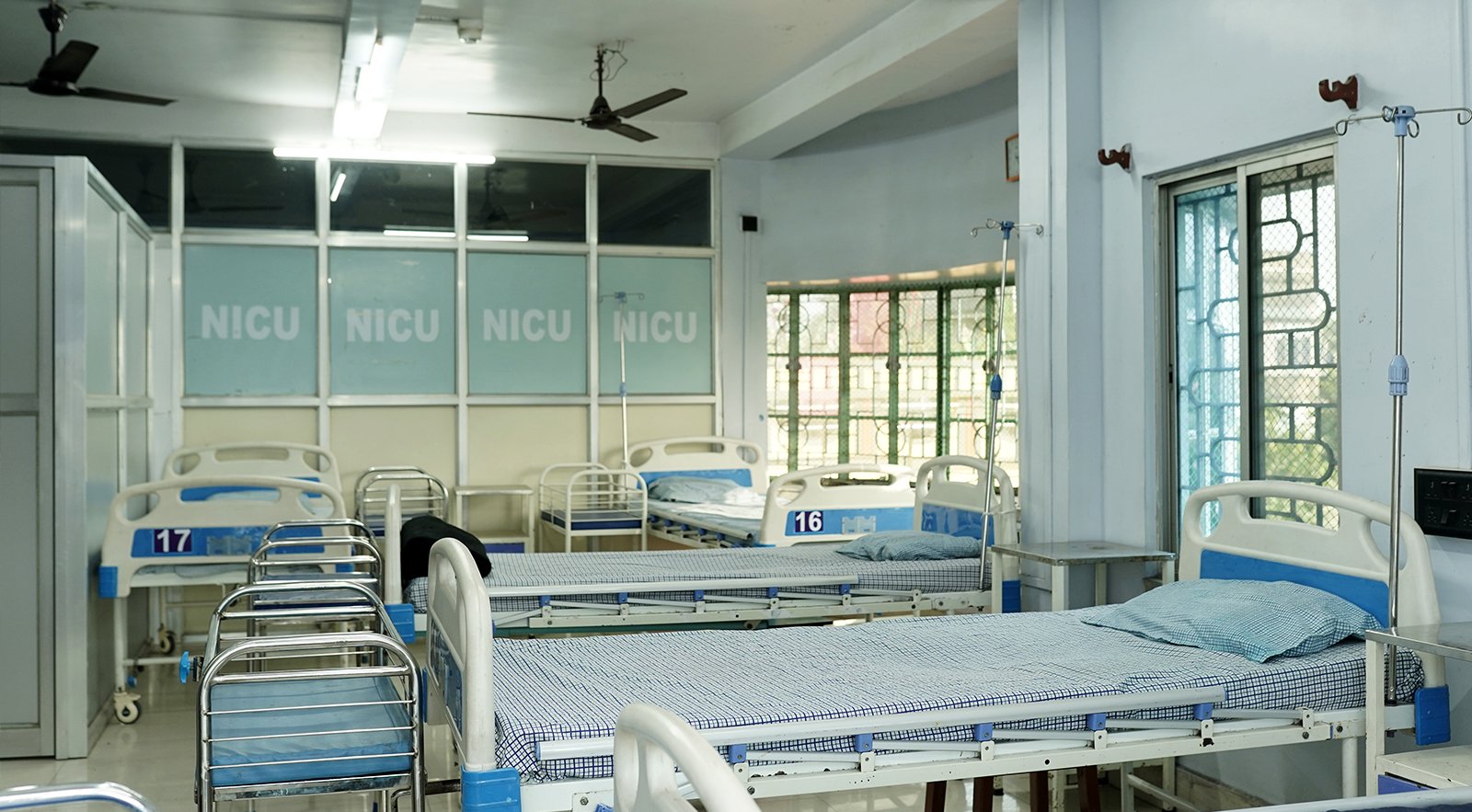 A clean and well-equipped NICU ward with multiple empty beds, medical stands, and large windows inside a nursing home.