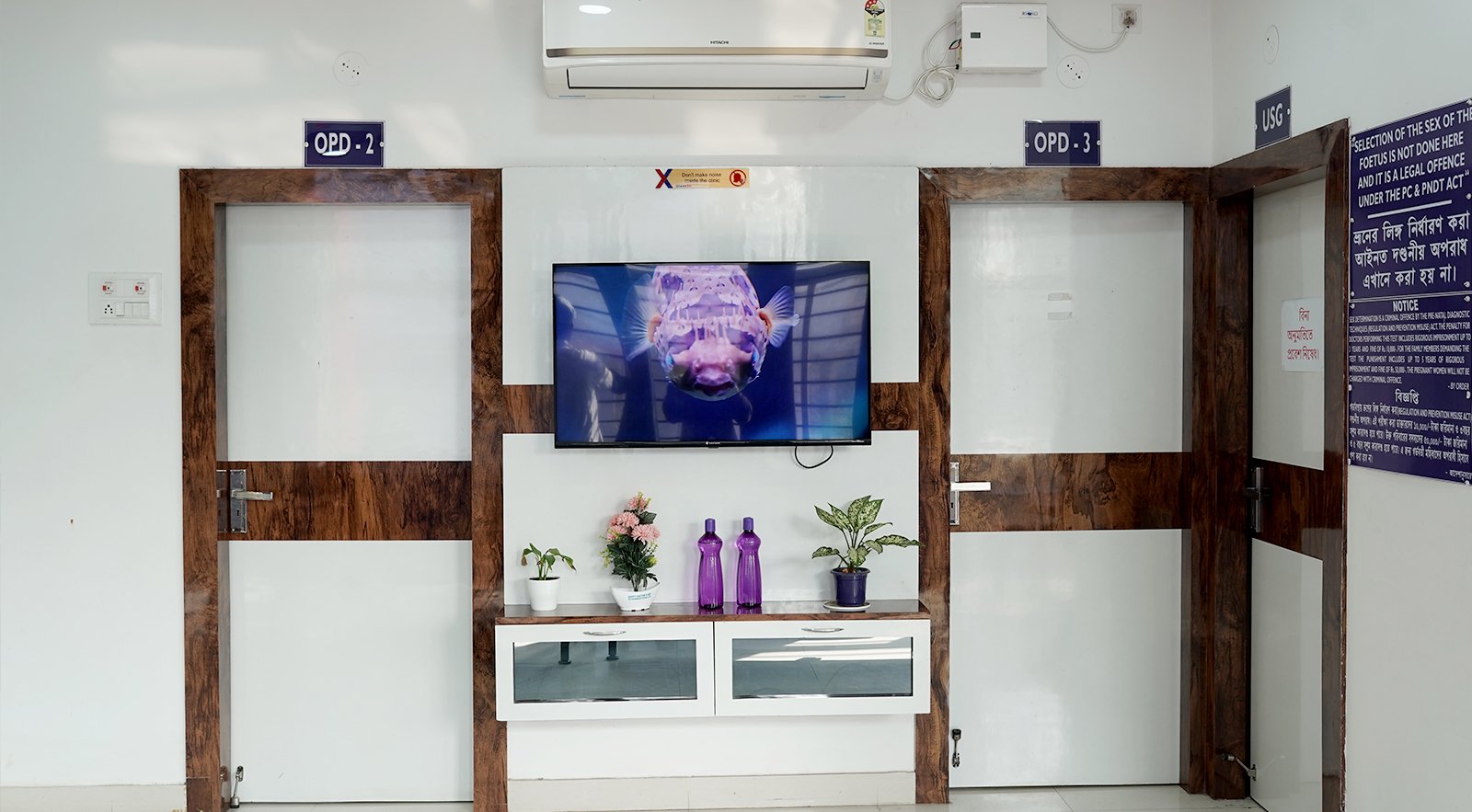 Nursing home waiting area with OPD rooms, wall-mounted television, wooden doors, and clean modern interior design.