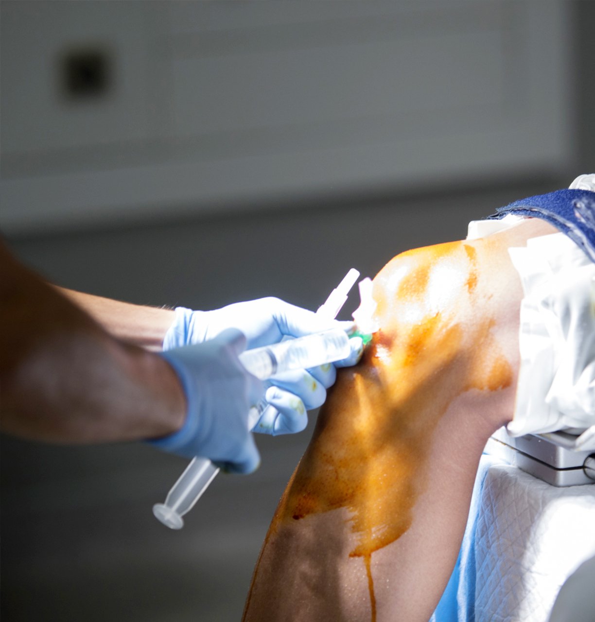 A doctor administering an injection into a patient’s knee under sterile conditions in a nursing home.